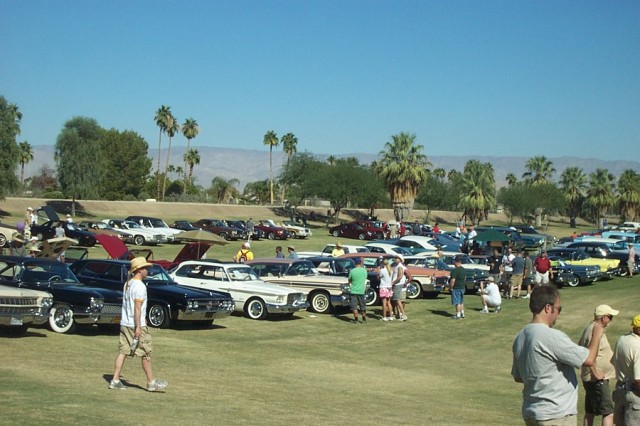 Classic cars parked on a grassy lawn at an outdoor car shown with viewers walking around the cars.